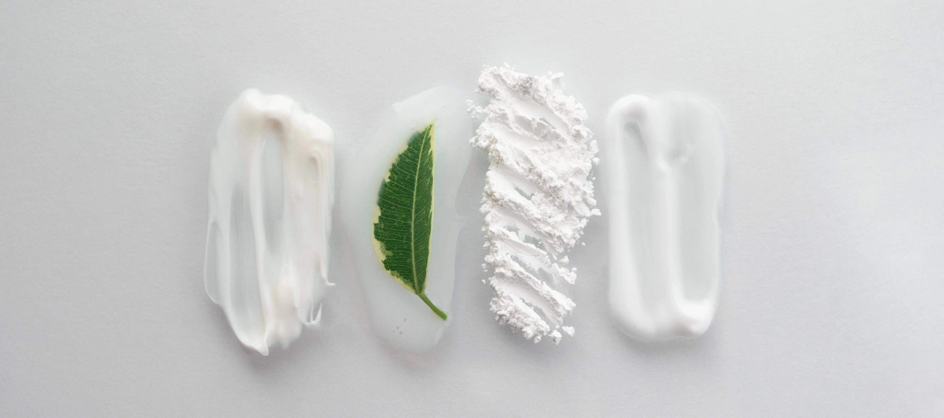 Four streaks of white cream with a green leaf on a light gray background