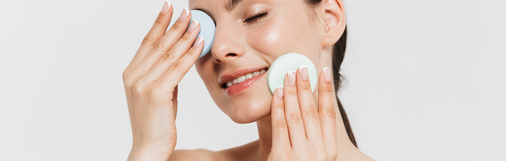 Woman applying a facial product with cotton pads on a plain background