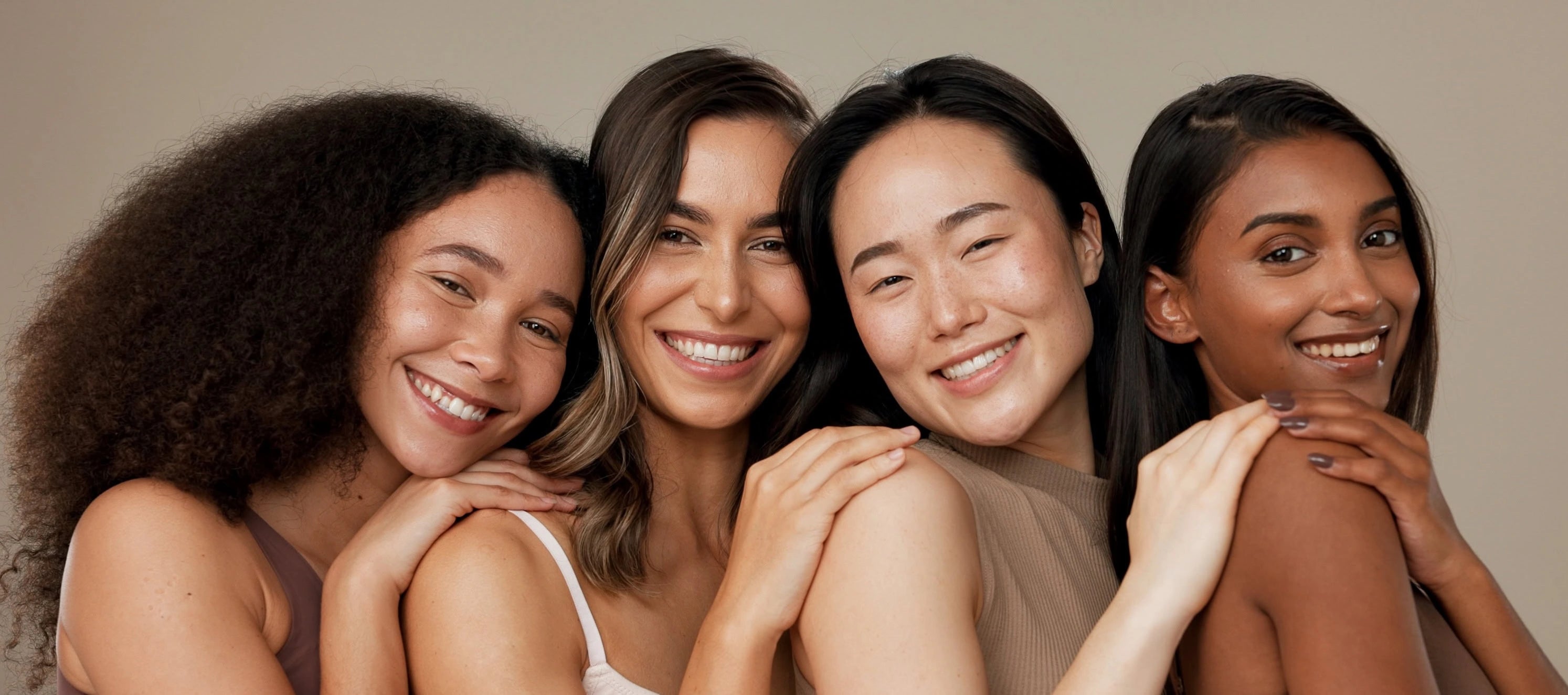 Four women with different hair types and skin tones smiling together against a beige background