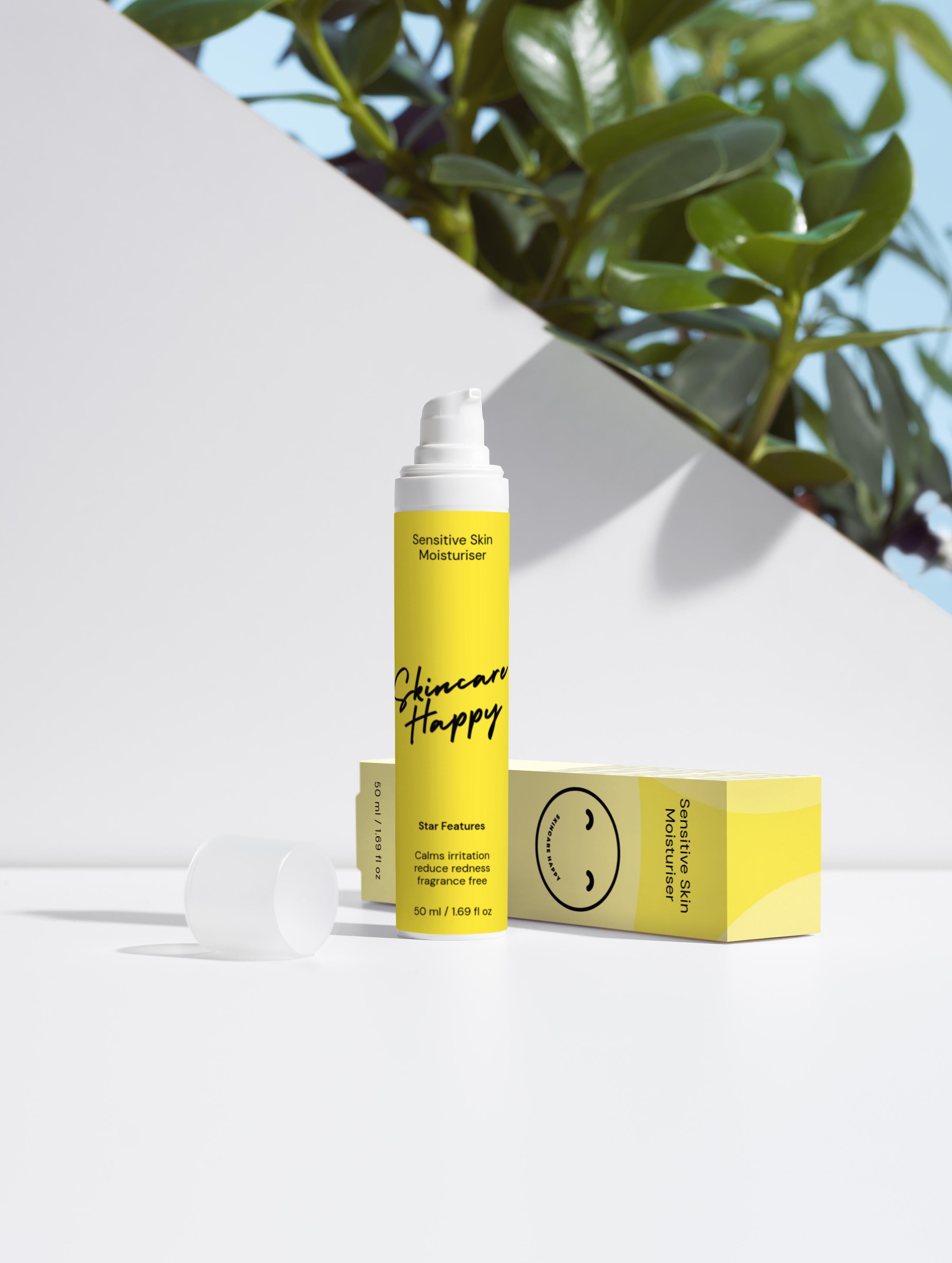 Skincare Happy product with yellow packaging on a white surface with green leaves in the background