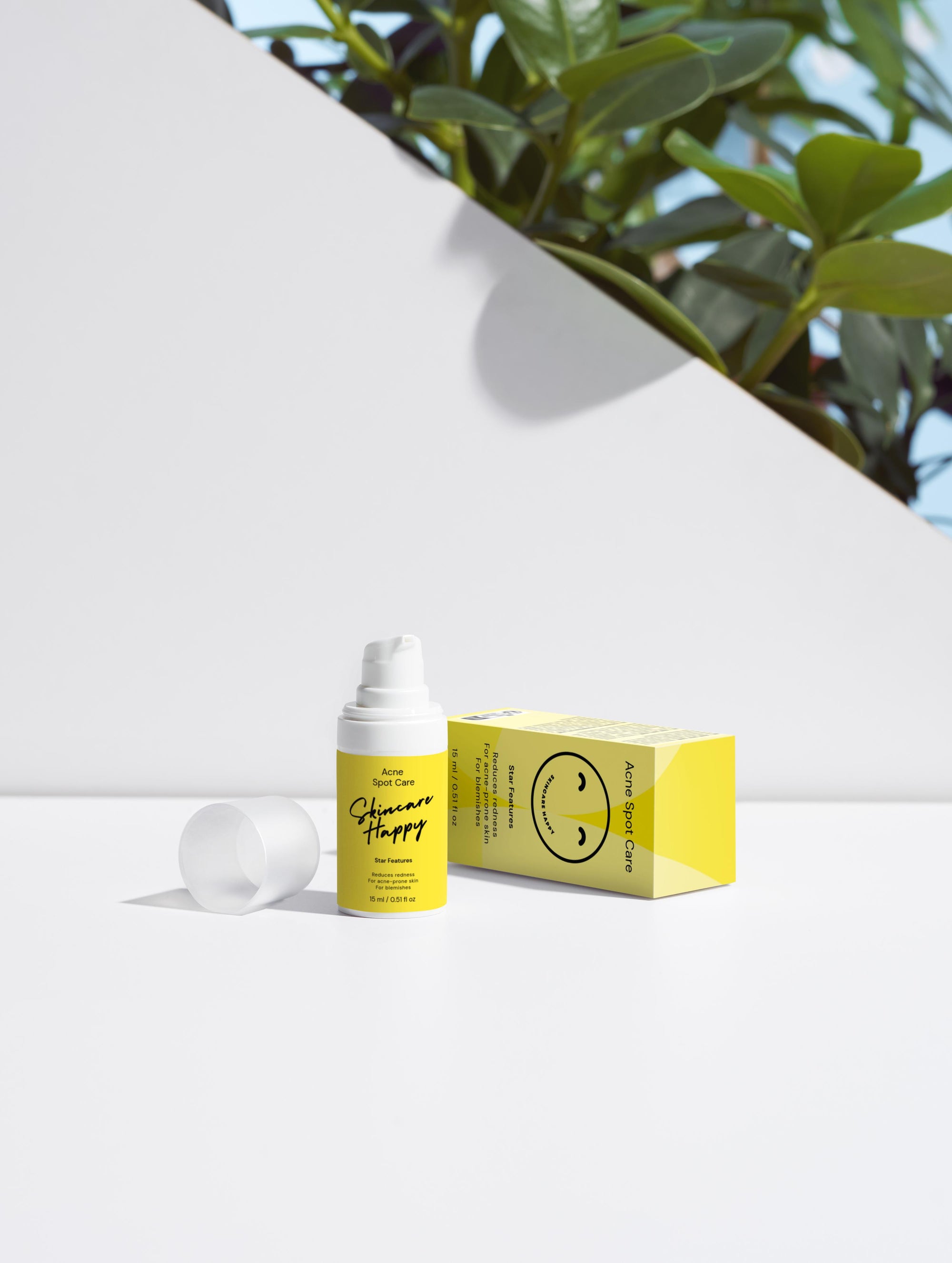 Skincare bottle and box with a smiley face design on a white surface with greenery in the background