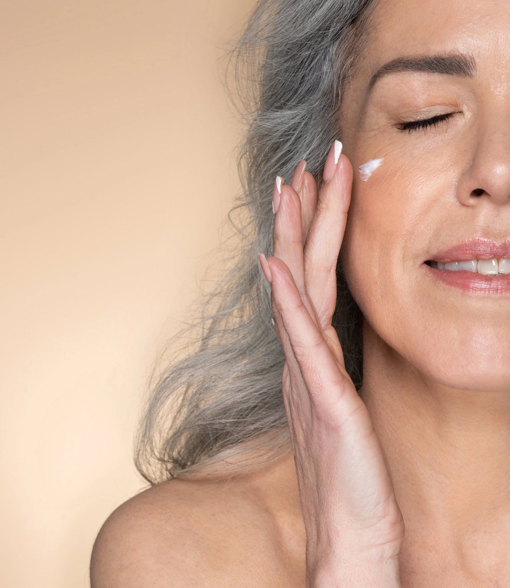 Woman applying cream to her face with a beige background