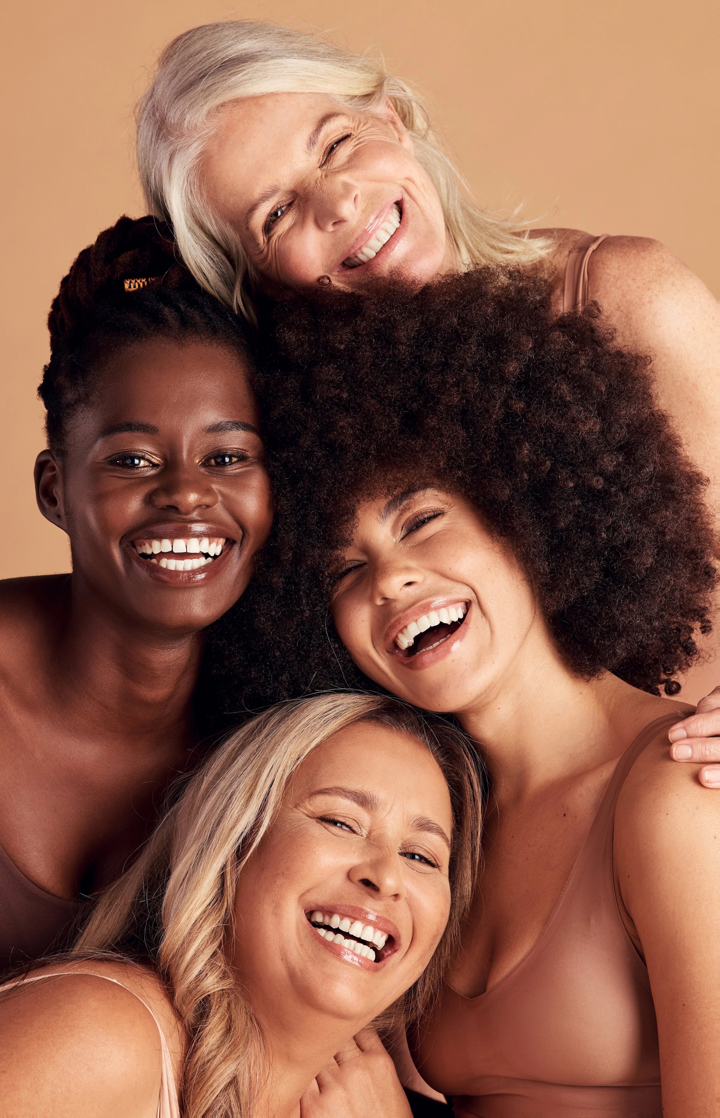 Four women with different hair types and skin tones smiling together against a beige background