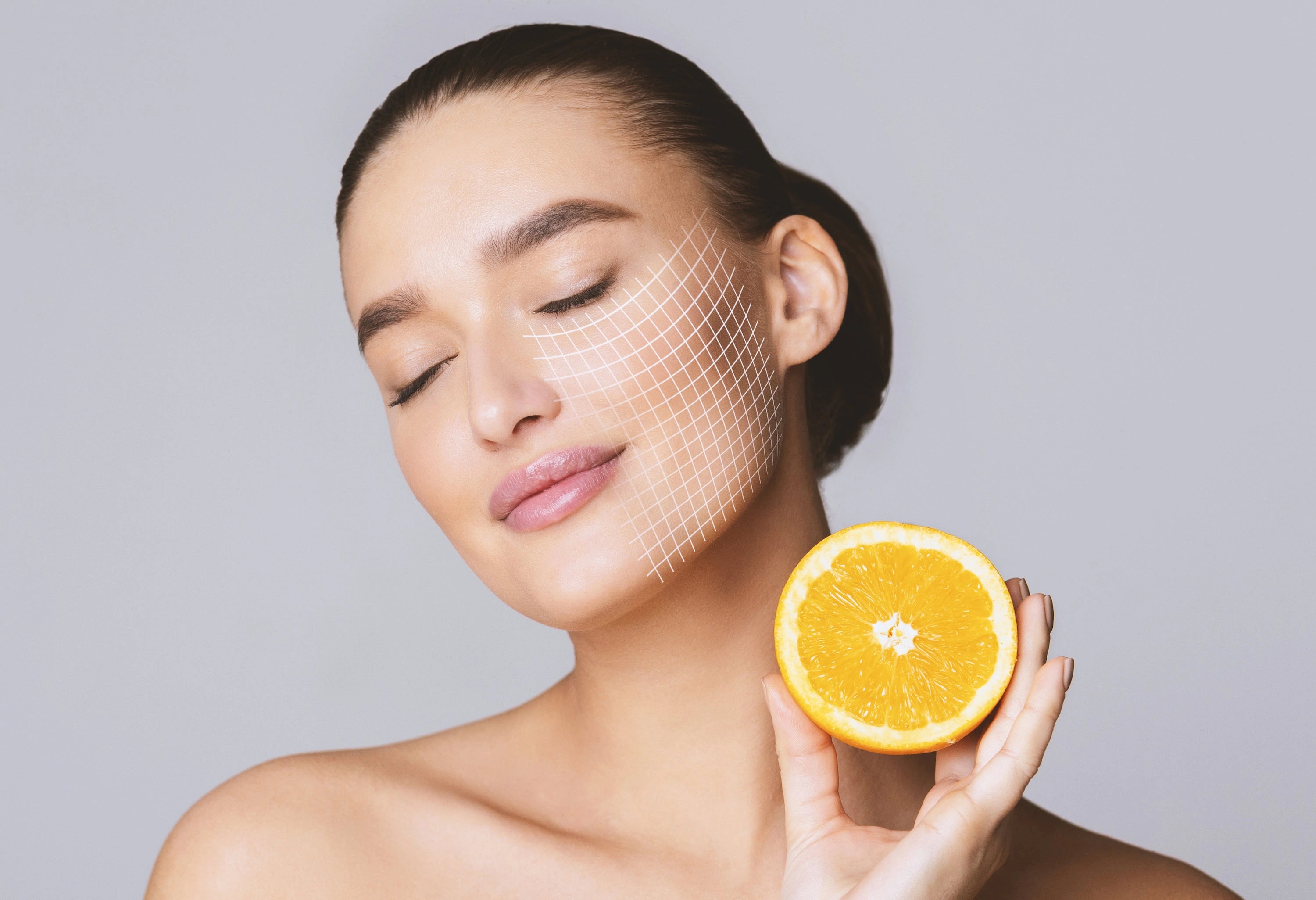 Woman holding an orange with a digital grid overlay on her face against a gray background
